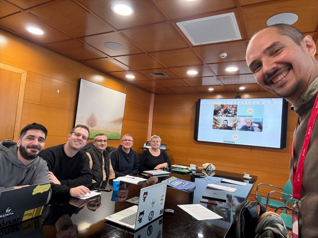 Partners from the MOSAIC project seated around a conference table during a focus group session, with additional partners visible on a screen joining via a video conference call.